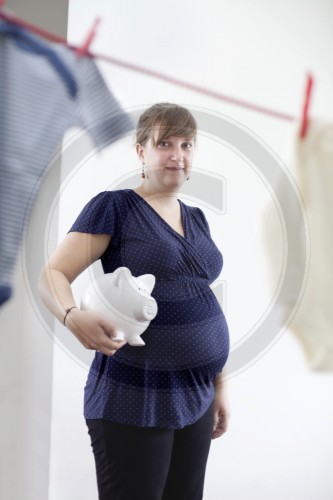 Schwangere Frau haelt ein Sparschwein