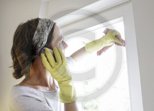 Hausfrau putzt Fenster und telefoniert