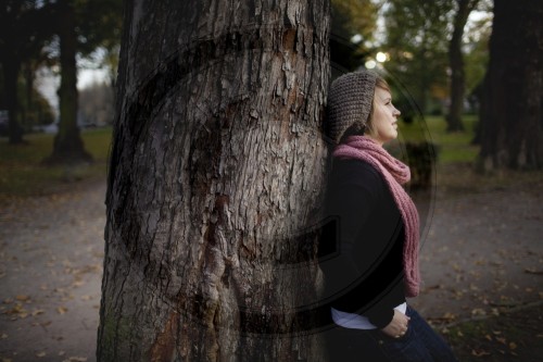 Junge Frau lehnt an einem Baum