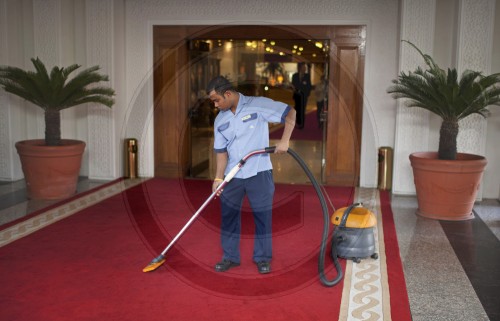 Mitarbeiter eines Hotels saugt den roten Teppich | Employee of a hotel hoovering the red carpet