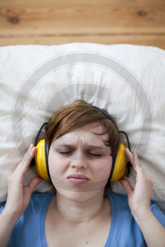 Junge Frau mit Gehoerschutz im Bett | Young woman with ear protection in bed