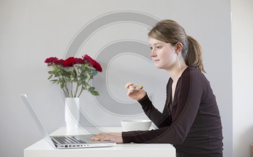 Junge Frau mit Laptop und Mueslischale.