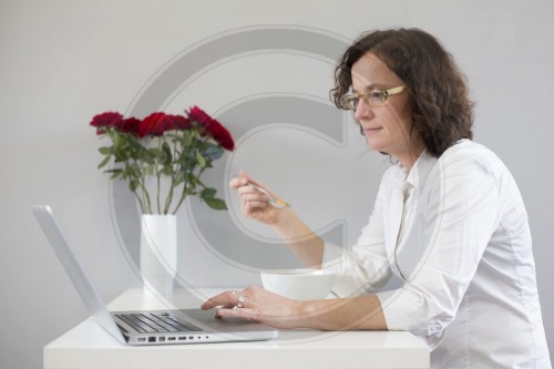 Frau mit Laptop und Mueslischale.