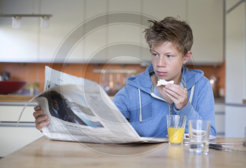Jugendlicher liest Zeitung beim Fruehstueck