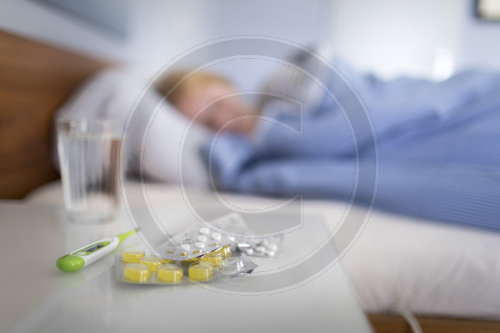 Tabletten im Vordergrund und Frau liegt krank im Bett