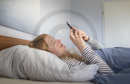 Frau liegt mit Mobiltelefon im Bett