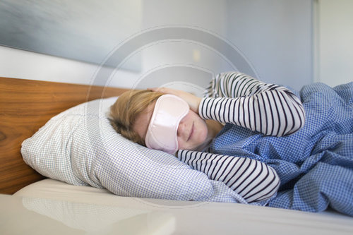 Frau liegt mit Augenbinde im Bett