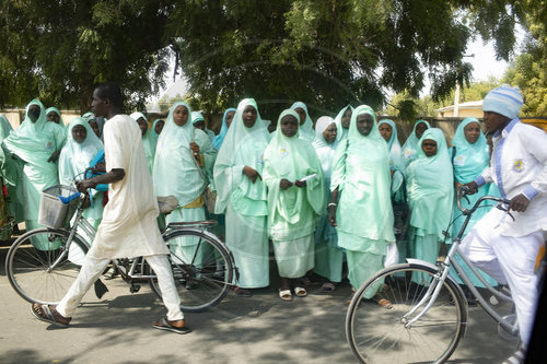 Frauen in gruenen Gewaendern und Radfahrer in Maiduguri