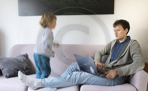 Vater mit  Kind arbeitet auf dem Sofa