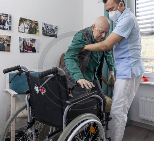 Alter Mann wird in einen Rollstuhl geholfen