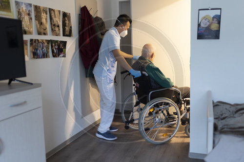 Altenpfleger schiebt einen Rollstuhl im Pflegeheim durch eine Tuer