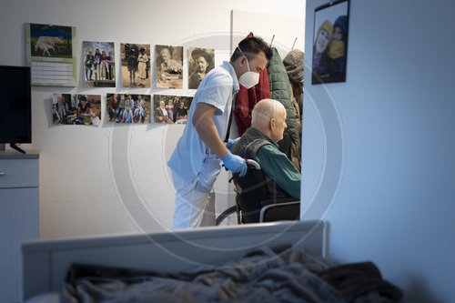 Altenpfleger schiebt einen Rollstuhl im Pflegeheim durch eine Tuer