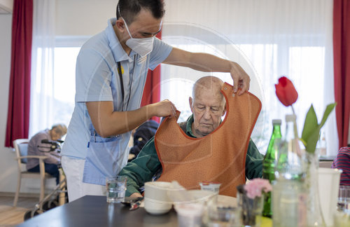 Pfleger legt einem Mann ein Laetzchen an im Pflegeheim