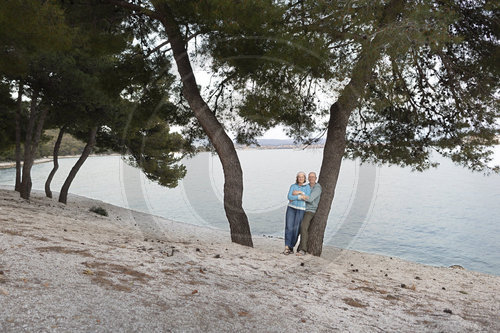 Paar lehnt an einem Baum am Meer