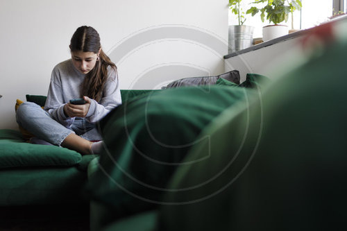 12 jaehriges Maedchen mit einem Smartphone auf dem Sofa