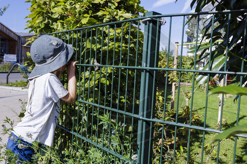 Ein Kind guckt durch den Zaun in einen Garten